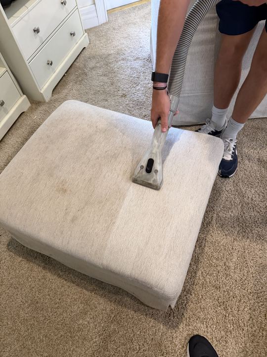 Cream fabric ottoman half cleaned, showing the dirty and clean halves